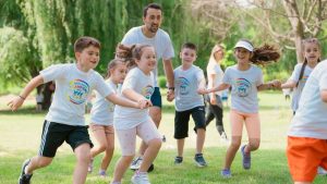 Children joyfully running and holding hands in a sunny park, enjoying outdoor recreation.